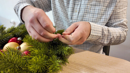A Caucasian man decorates a Christmas wreath with red and gold ornaments, embodying holiday preparation and festive creativity