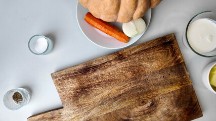 Top view of ingredients for a creamy autumn pumpkin soup on a wooden cutting board, ideal for Thanksgiving recipes