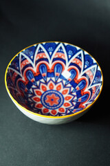 A side perspective of a decorative ceramic bowl with vivid geometric designs in blue, red, and white, bordered by a striking yellow edge.
