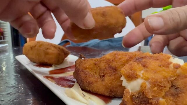 close-up view of the hands of a caucasian man eating traditional homemade serrano ham croquettes in a bar.