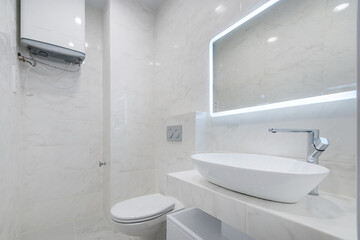 Elegant design of the bathroom, decorated in white. Illuminated mirror over the sink. .Installed water heater.