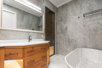 Bathroom with modern interior design. Marble tiles. Exclusive bathtub, wooden cabinet with sink.