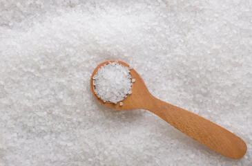 Coarse table salt in a wooden spoon background. Top view