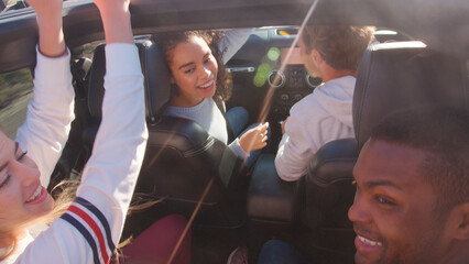 Close Up Of Group Of Young Friends On Road Trip Driving In Convertible Car