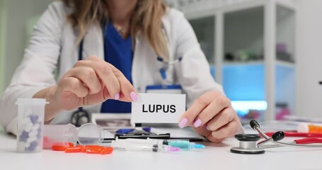 Female medical professional displays Lupus word on small paper sheet. Therapist diagnoses autoimmune disease to patient in hospital office