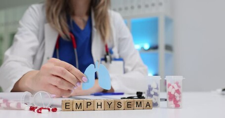 Word Emphysema and healthcare worker holding paper lungs cut model over table. Woman doctor represents respiratory disease awareness in hospital