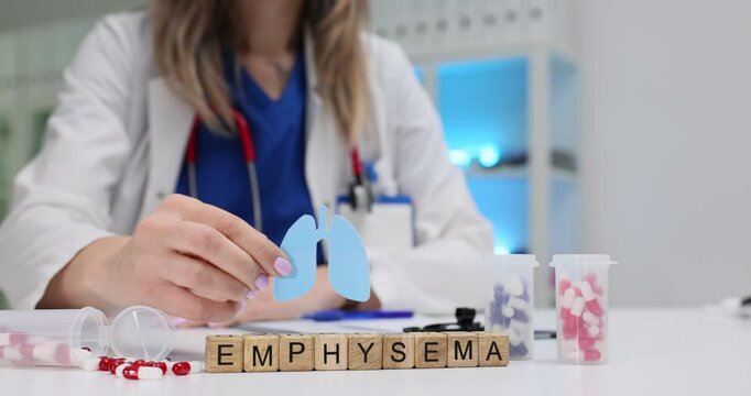 Word Emphysema and healthcare worker holding paper lungs cut model over table. Woman doctor represents respiratory disease awareness in hospital