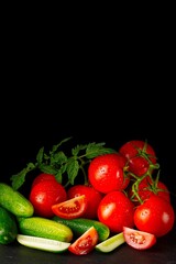 A stunning variety of fresh organic vegetables, including vibrant tomatoes and crisp cucumbers, arranged beautifully on a black background, showcasing their natural colors and textures.