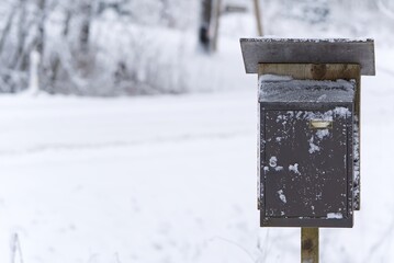 A charming retro style dark brown wooden mailbox stands elegantly on a snowy roadside during winter. The mailbox, adorned with a small American flag, contrasts beautifully with the white snow.