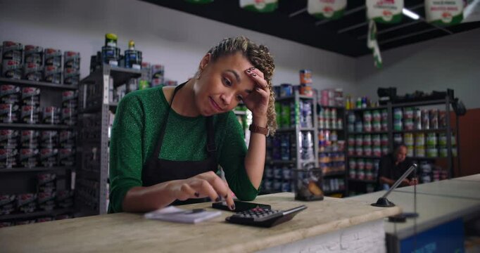 Female entrepreneur looking frustrated while calculating finances at a small business counter, managing financial challenges in a retail setting