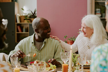 Medium close up of senior Caucasian elegant woman caressing her beloved African American husband while enjoying meal and looking at her
