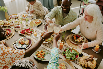 High angle shot of biracial family clinking glasses with champagne while enjoying family dinner