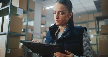 Female Logistics Specialist Uses Tablet Computer, Checks Inventory, Processes Online Orders for Delivery. Warehouse Employee Working in the Background. Sorting Center of E-Commerce Store. Dolly Shot.