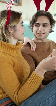 Vertical video: Couple wearing reindeer antlers enjoying cozy holiday moment with hot drinks