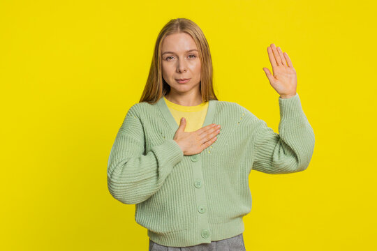 I swear to be honest. Sincere responsible Caucasian young woman 40 years old raising hand to take oath, promising to be honest, to tell truth, keeping hand on chest, justice. Girl on yellow background - Powered by Adobe