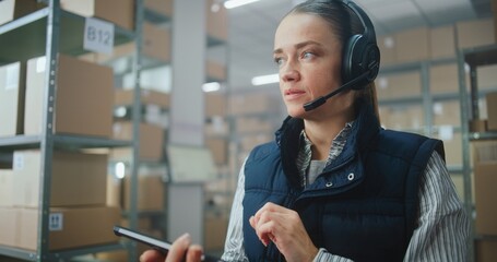 Female Logistics Coordinator, Manager Wearing Headset Chats to Customer, Uses Tablet Computer in...