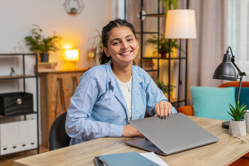 Young woman sitting at table closing laptop after finishing work in living room. Happy Indian girl...