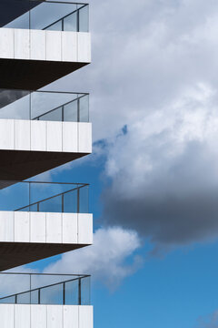 A striking view of modern architecture featuring multiple balconies, framed by a beautiful blue sky and clouds, emphasizing contemporary design elements and aesthetics.