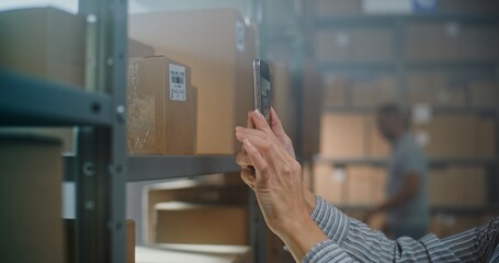 Close Up of Warehouse Associate Scanning Cardboard Box with E-Commerce Online Order in Sorting Center Using Smartphone, Taking Parcel from Rack for Shipping to Customer. Postal Delivery Service.