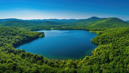 Obraz premium A serene lake reflects the bright blue sky, embraced by rolling green hills and majestic mountains. The peaceful atmosphere invites exploration and appreciation of nature's beauty