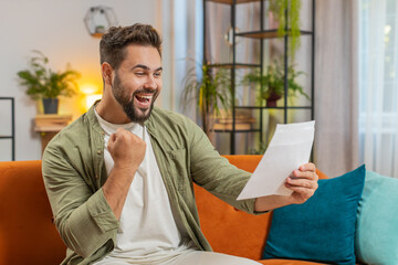 Fototapeta premium Happy man with brown hair open envelope letter, reading it. Career growth advance promotion, bank loan approve, successful admission to university monetary award invitation great news, lottery win.
