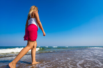 Beautiful middle-aged woman walking on sandy beach in summertime. Physical activity on beach. Side view	