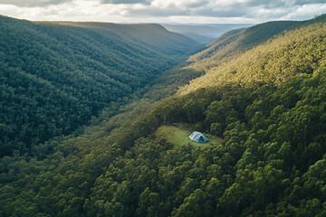 Lush green mountains surrounding a solitary cabin in the valley during overcast weather