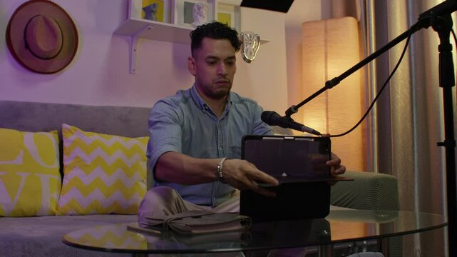 A man sets up a podcast studio at home with a microphone, tablet, and cozy decor