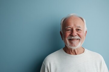 Obraz premium Half body shot of a senior man, smiling warmly, against a solid pale blue background with space for additional text