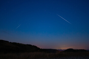 Countryside silhouettes under the stars, Milky Way and meteor shower.