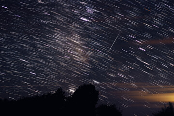 Milky Way stars with meteor shower trails and countryside silhouettes.