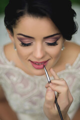 A woman is applying lipstick with a brush. The image is blurry and has a soft, romantic feel to it