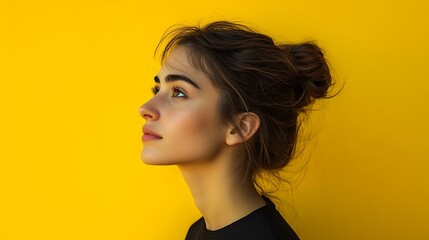 Young woman with bun hairstyle, profile view against vibrant yellow background.