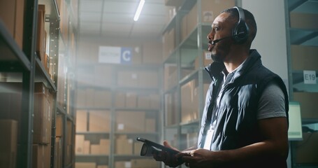 African American Logistics Coordinator in Headset Chats with Customer, Uses Tablet Computer, Looks...