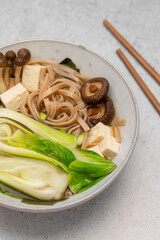 Traditional Japanese Miso soup with Wakame seaweed, tofu cheese, shiitake and enoki mushrooms, soba noodles and pak choi with chopsticks for single serving. Vegetarian, vegan and healthy concept.