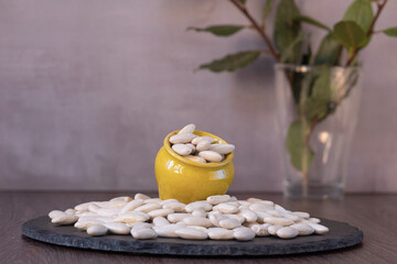 Large white beans spilling from yellow ceramic pot onto slate plate