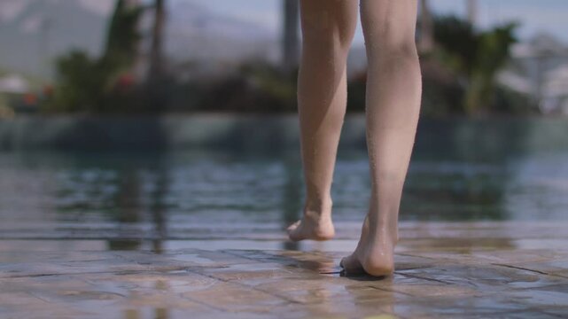Young woman entering the pool. Young girl wearing a colorful swimsuit enters the pool in the garden. High quality video shooting with a fixed camera