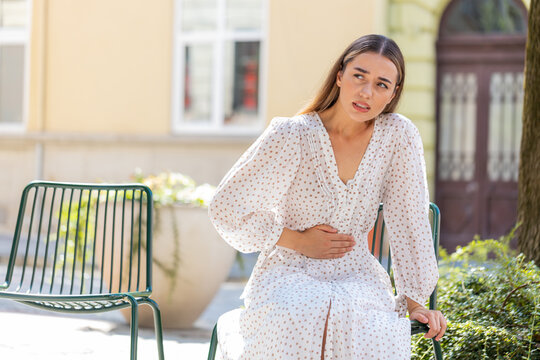 Caucasian young woman traveler feeling sudden strong abdominal stomach ache gastritis problem. Upset tourist lady having symptom poisoning diarrhea indigestion peptic ulcer pancreatitis on city street