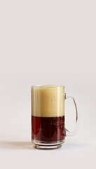 Kvass in a glass, light background. Glass of dark beer or kvass with foam in a glass on a light gray background. Traditional beer mug with a handle. Close-up on a glass with a cool tasty drink