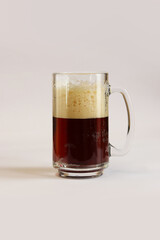 Kvass in a glass, light background. Glass of dark beer or kvass with foam in a glass on a light gray background. Traditional beer mug with a handle. Close-up on a glass with a cool tasty drink