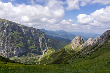 Obraz premium A mountainous area with jagged peaks partially covered with snow and green slopes, white clouds can be seen in the sky.
