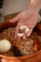 Cook adding garlic cloves to a traditional Asturian fabada dish