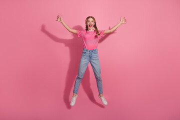 Happy young woman in casual summer outfit jumping against pink background with a joyful expression and red lipstick.