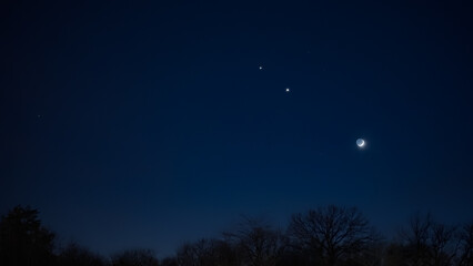 Crescent young Moon with stars, planets and countryside silhouettes.