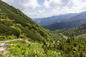 
A hilly area with green slopes with paths winding down to a valley where a small lake glistens.