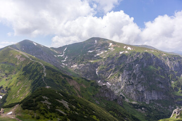 
A mountain range with snow-capped peaks, steep slopes and green valleys covered with rare trees and shrubs.