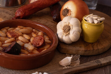 Asturian fabada ingredients surrounding a clay pot on a wooden table