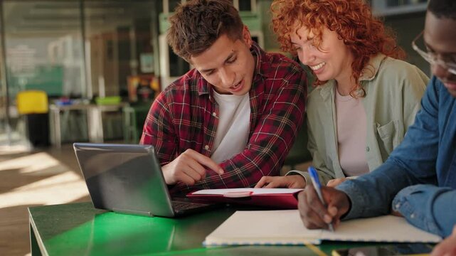 Young university students helping each other learn. Teamwork tutoring for exams with books and laptop at college library