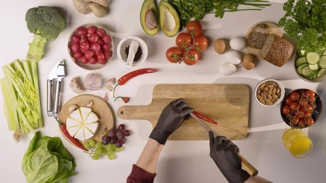 Przygotowanie czerwonej papryki na desce do krojenia otoczonej świeżymi warzywami i produktami na białym stole kuchennym