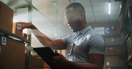 African American Warehouse Associate Scans Cardboard Box with E-Commerce Online Orders Using Tablet...
